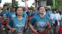 Sebanyak 144 pelari ambil bagian dalam Sudaji Peace Trail Fun Run 2026 yang digelar di Desa Sudaji, Kecamatan Sawan, Kabupaten Buleleng. Menempuh jarak sekitar 6 kilometer, para peserta tidak hanya diajak berolahraga, tetapi juga menikmati indahnya persawahan dan kehidupan pedesaan sekaligus terlibat dalam aksi kepedulian terhadap lingkungan melalui penaburan eco enzyme di sejumlah kawasan seputaran Desa Sudaji. Kegiatan ini dilepas secara langsung oleh Ketua TP-PKK Provinsi Bali, Ny. Putri Koster bersama Ketua (Himpunan Kerunan Tani Indonesia) HKTI Provinsi Bali, Gede Muliawan Arya dan Wakil Bupati Buleleng, Gede Supriatna di Lapangan Desa Sudaji, Minggu, (20/9). Gubernur Bali dalam sambutannya yang dibacakan oleh Kepala Dinas Pariwisata Provinsi Bali, I Wayan Sumarjaya menyampaikan apresiasi kepada panitia, Kelompok Sadar Wisata (Pokdarwis) Desa Sudaji, masyarakat, komunitas, dan seluruh pihak yang telah menggagas kegiatan tersebut. Menurutnya, Sudaji Peace Trail Fun Run 2026 bukan sekadar kegiatan olahraga, melainkan sebuah cara untuk memperkenalkan kekayaan alam dan kehidupan masyarakat pedesaan kepada peserta sekaligus menggerakkan perekonomian lokal. “Ini adalah cara kita berolahraga sambil menikmati alam, mengenal kehidupan masyarakat desa, menggerakkan ekonomi lokal, sekaligus mengingatkan kembali kepada kita semua tentang pentingnya menjaga lingkungan dan budaya Bali,” ujarnya. Desa Sudaji memiliki potensi yang sangat besar untuk pengembangan pariwisata berbasis masyarakat. Hamparan persawahan, lingkungan yang asri, aktivitas pertanian, budaya, tradisi, hingga kehidupan masyarakat menjadi kekuatan yang dapat dikembangkan sebagai pengalaman wisata yang autentik. Melalui kegiatan tersebut, peserta tidak hanya datang untuk berlari, tetapi juga diajak merasakan suasana Bali secara lebih dekat. Mulai dari menikmati udara pagi pedesaan, menyaksikan hamparan sawah, berinteraksi dengan masyarakat, hingga mencicipi kuliner lokal dan mengenal produk UMKM. “Bali bukan hanya tentang tempat yang indah untuk dikunjungi, tetapi juga kehidupan budaya, alam, dan masyarakat yang memberikan pengalaman kepada setiap wisatawan,” tegasnya. Ia juga menekankan bahwa pengembangan sport tourism harus berjalan beriringan dengan keberlanjutan lingkungan. Menurutnya, ketika masyarakat dan wisatawan menikmati keindahan alam, maka tanggung jawab untuk menjaganya juga harus menjadi bagian dari setiap aktivitas. Karena itu, konsep eco-friendly yang diusung dalam Sudaji Peace Trail Fun Run 2026 dinilai menjadi langkah positif. Termasuk semangat penggunaan pupuk organik, pelestarian ekosistem persawahan, aksi penanaman pohon, serta penaburan eco enzyme sebagai bagian dari rangkaian kegiatan. “Ini adalah contoh sederhana bahwa sport tourism dapat berjalan bersama dengan environmental sustainability,” ujarnya. Kegiatan tersebut juga dinilai sejalan dengan semangat Nangun Sat Kerthi Loka Bali, yakni pembangunan yang menjaga keseimbangan dan keharmonisan antara alam, manusia, dan kebudayaan. Keberadaan sawah dan sistem subak tidak hanya dipandang sebagai bagian dari pariwisata, tetapi juga sebagai warisan pengetahuan, nilai, kebersamaan, dan kearifan masyarakat Bali dalam menjaga hubungan harmonis antara manusia dengan alam. Pihaknya berharap kegiatan seperti Sudaji Peace Trail Fun Run dapat terus berkembang dan menjadi bagian dari Calendar of Event pariwisata berbasis desa di Kabupaten Buleleng. Dengan demikian, kegiatan tersebut dapat secara konsisten menarik wisatawan, komunitas olahraga, maupun wisatawan minat khusus untuk datang dan menikmati potensi Desa Sudaji. Sementara itu, Wakil Bupati Buleleng, Gede Supriatna menyampaikan dukungan dan apresiasi Pemerintah Kabupaten Buleleng terhadap kegiatan yang diprakarsai Pokdarwis dan kelompok tani Desa Sudaji tersebut. Ia menilai Desa Sudaji merupakan salah satu desa wisata unggulan di Buleleng yang telah dikenal luas, bahkan telah memperoleh berbagai penghargaan hingga tingkat Internasional. “Ini tentu menjadi sebuah aset bagi Kabupaten Buleleng untuk bagaimana mendukung kegiatan-kegiatan yang dilaksanakan oleh Desa Sudaji, khususnya dari kelompok sadar wisata,” ujarnya. Wabup Supriatna berharap semangat dan komitmen dalam mengembangkan Desa Sudaji dapat terus dipertahankan sekaligus menjadi inspirasi bagi desa-desa wisata lainnya di Kabupaten Buleleng. “Semoga terus berkomitmen dan konsisten menjadikan Sudaji ini sebuah desa wisata dan juga bisa memberikan inspirasi buat desa-desa yang lain yang ada di Kabupaten Buleleng,” harapnya. Melalui Sudaji Peace Trail Fun Run 2026, Desa Sudaji menunjukkan bahwa olahraga dapat menjadi pintu masuk untuk memperkenalkan potensi desa secara lebih luas. Ketika langkah para pelari menyusuri alam pedesaan berpadu dengan aksi menjaga lingkungan dan aktivitas ekonomi masyarakat, sport tourism tidak lagi sekadar tentang mencapai garis finis, tetapi juga tentang menghadirkan manfaat bagi alam dan masyarakat.